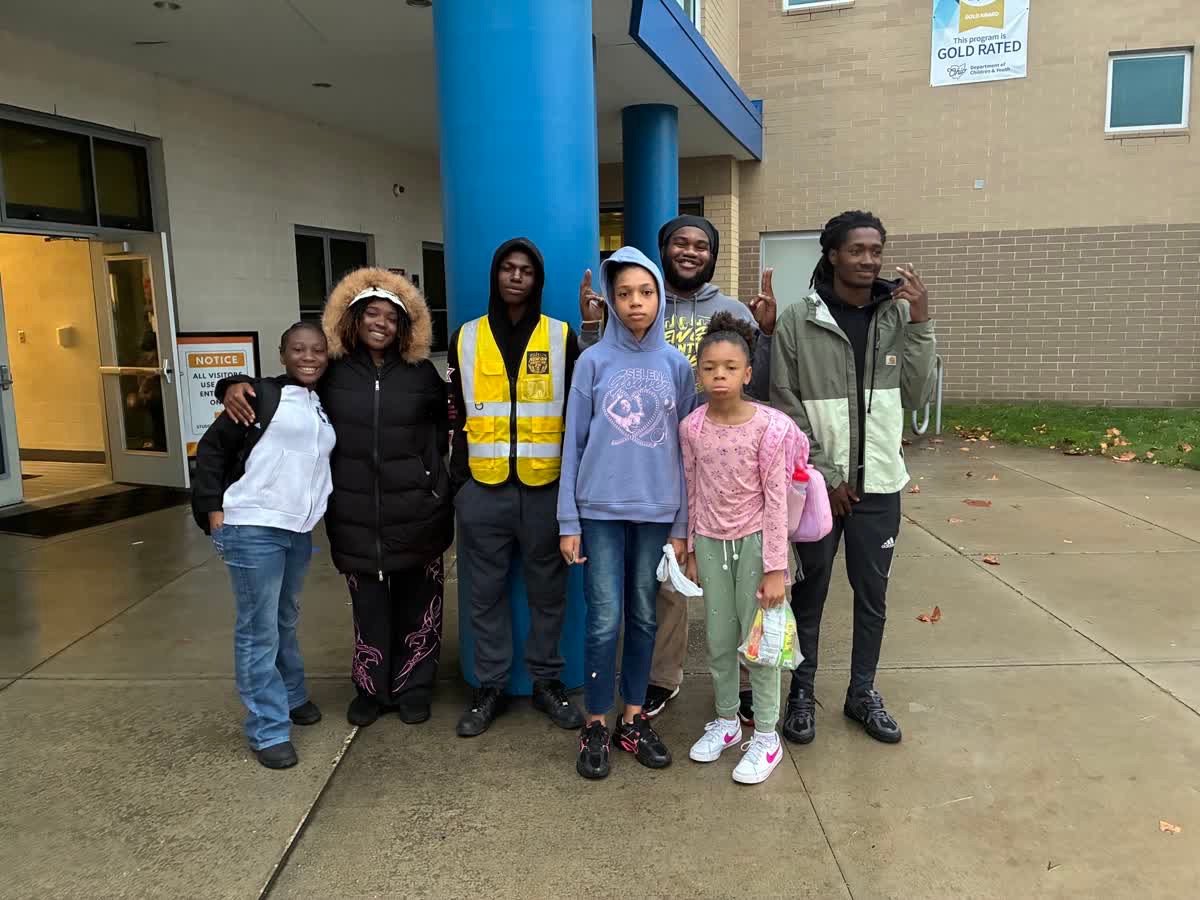 A group stands together outside an entrance with blue columns; one person wears a yellow safety vest.